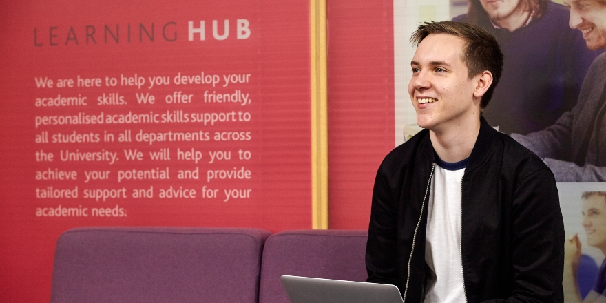 Blonde man with silver laptop sat on purple sofa 