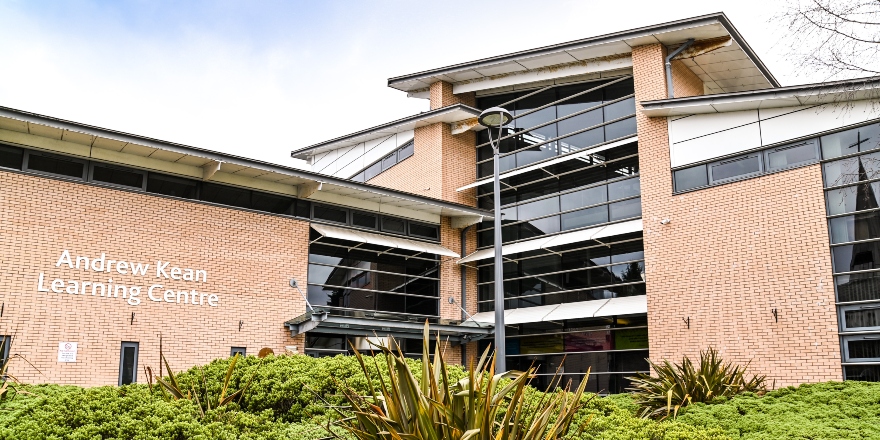 A brick library building with large windows, set behind greenery