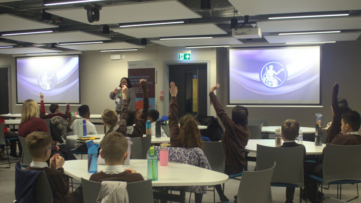 A picture of students raising their hands while sat in a classroom