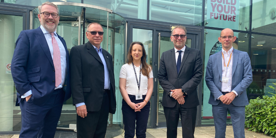 Four men and a woman stand in a line in front of glass building