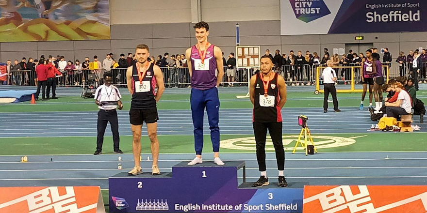 Three male athletes stand on podium