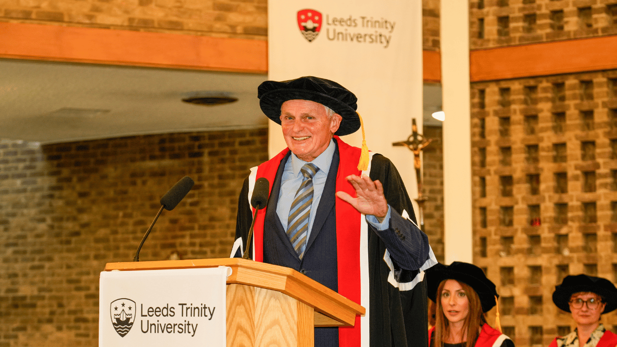 A male academic in cap and gown speaking at Leeds Trinity University.