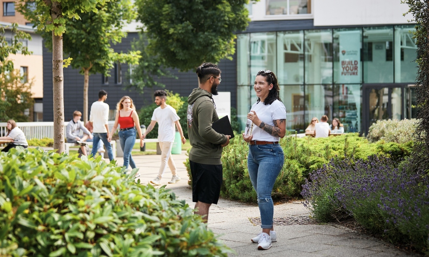 Two students outside on a green campus, in front of the Atrium
